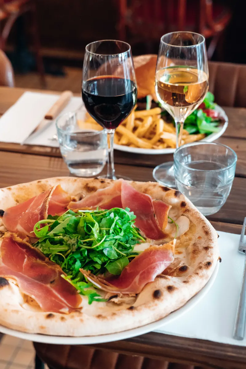 Pizza signée Pizzou au jambon et à la roquette servie au Botza, verre de vin